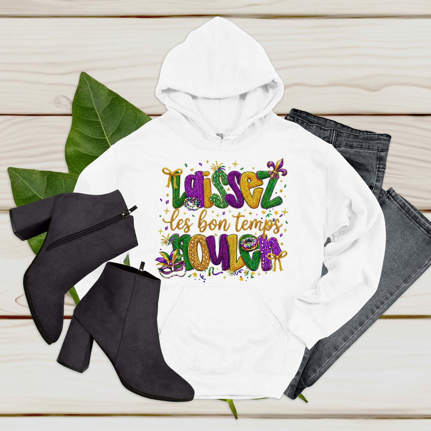 White hoodie with colorful text, black boots, and jeans on a wooden surface