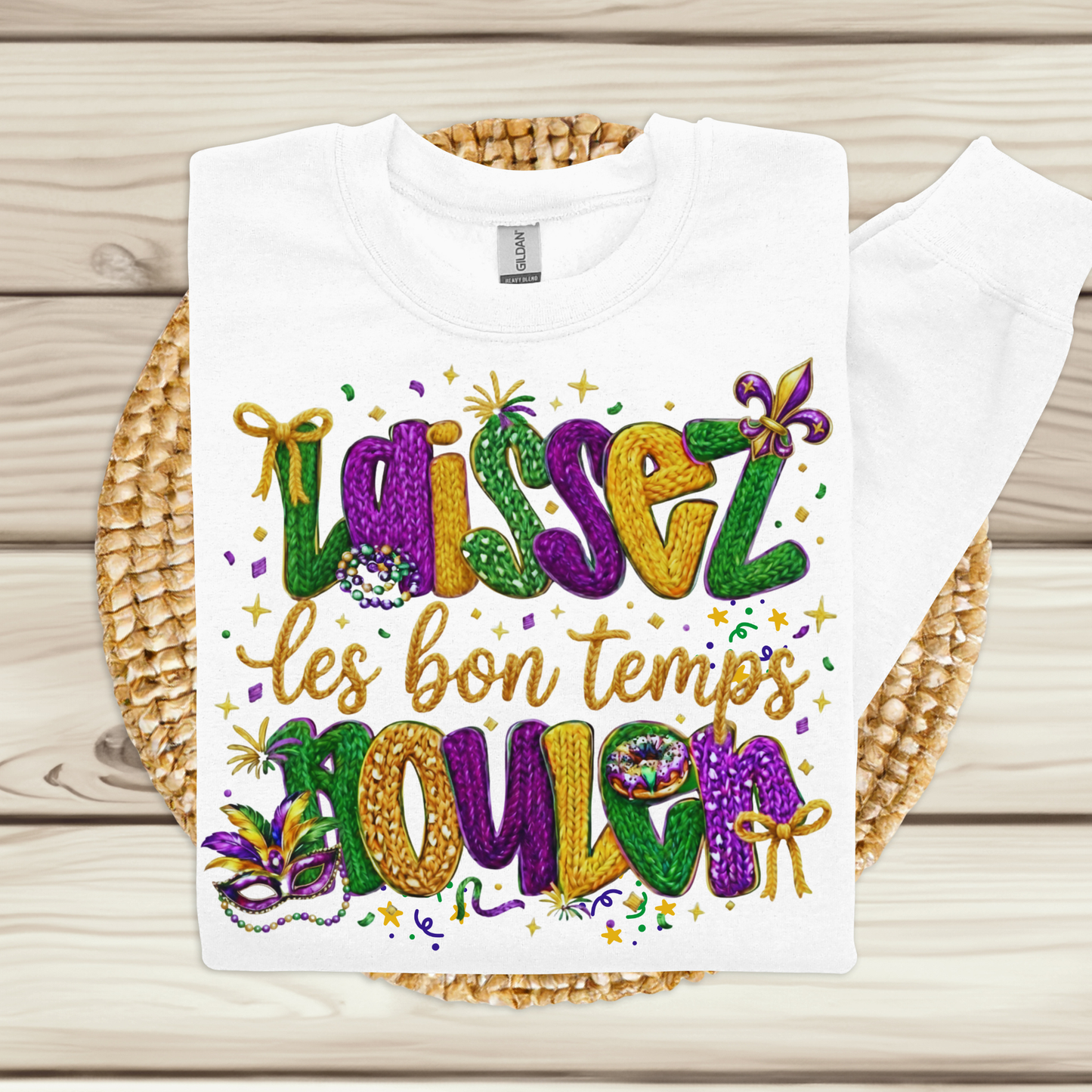 White t-shirt with colorful Mardi Gras-themed text on a woven mat.