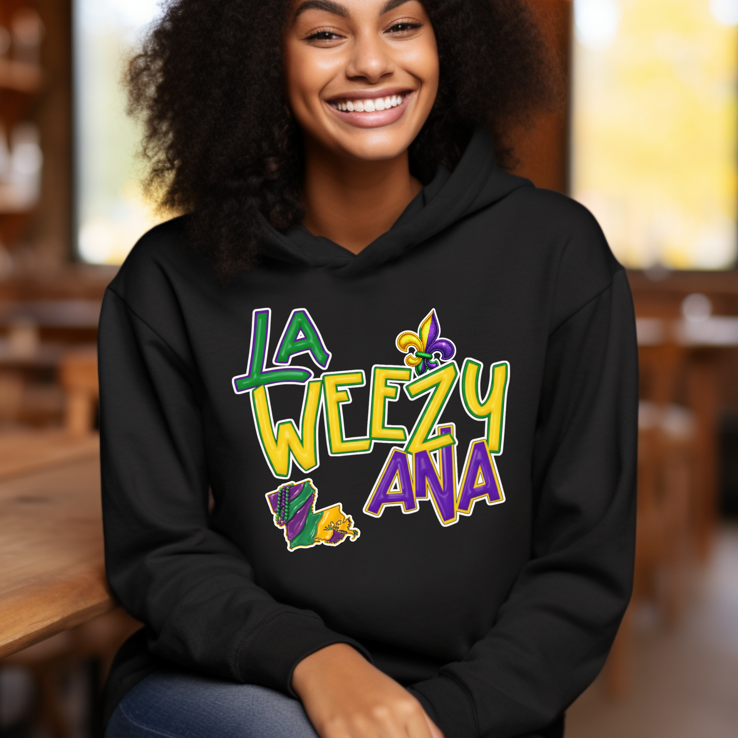 Person wearing a black hoodie with 'LA WEEZY ANA' text and graphics, sitting indoors.