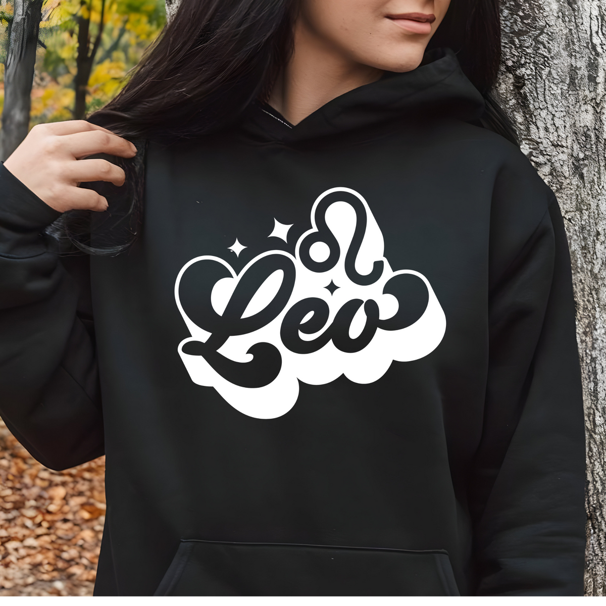 A person wearing a black hoodie with a large white 'm Scorpio' graphic on the chest, standing outdoors next to a tree trunk.