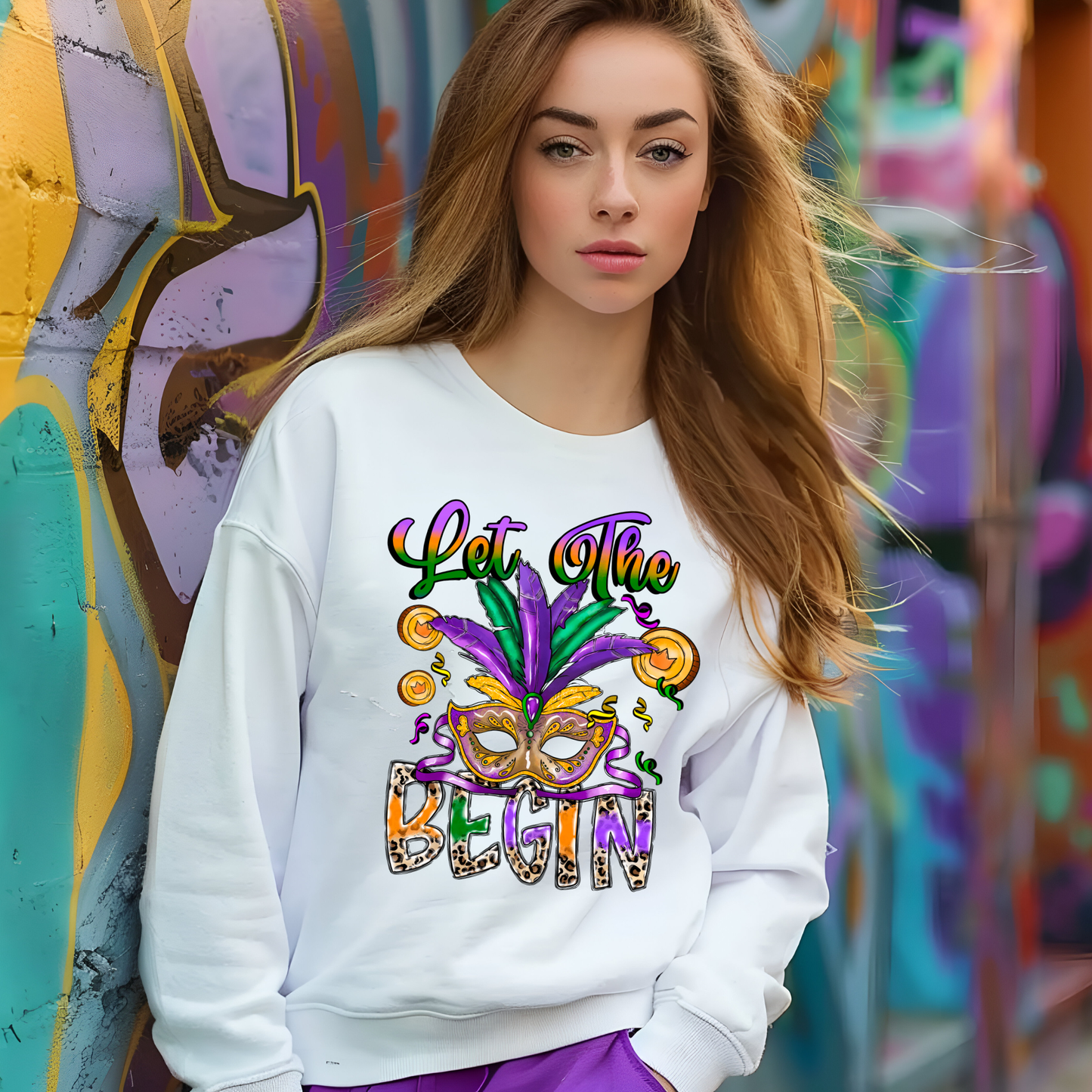 Woman wearing a white sweatshirt with colorful text and design, standing in front of a graffiti wall.