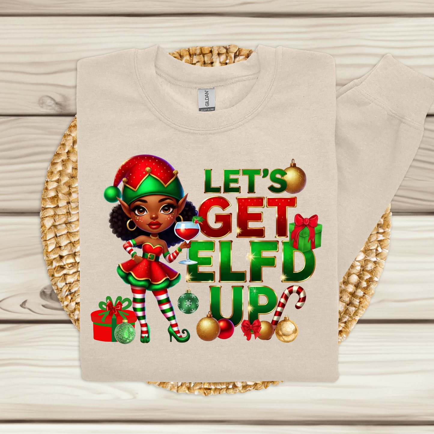 Beige sweatshirt with Christmas-themed design featuring an elf and text on a wooden surface.