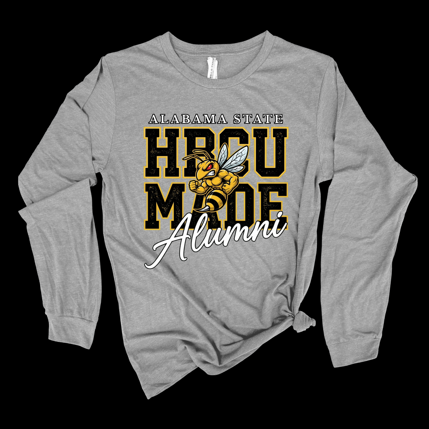A heather gray long-sleeve t-shirt with a graphic on the front that reads 'AL-ABAMA STATE HBCU MADE Alumni' in black, gold, and white, featuring a yellow and black hornet illustration. The shirt is laid flat against a solid black background.