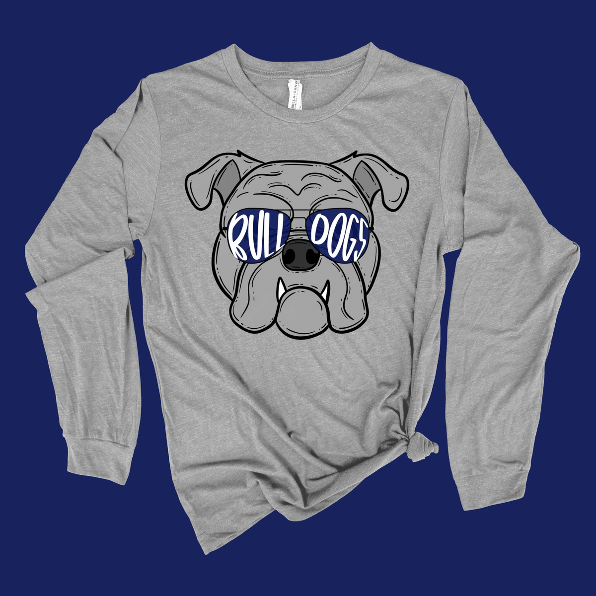 A heather gray long-sleeve t-shirt with a graphic of a bulldog wearing sunglasses that read 'RULL DOGS' in blue and white. The shirt is displayed flat against a solid dark blue background.