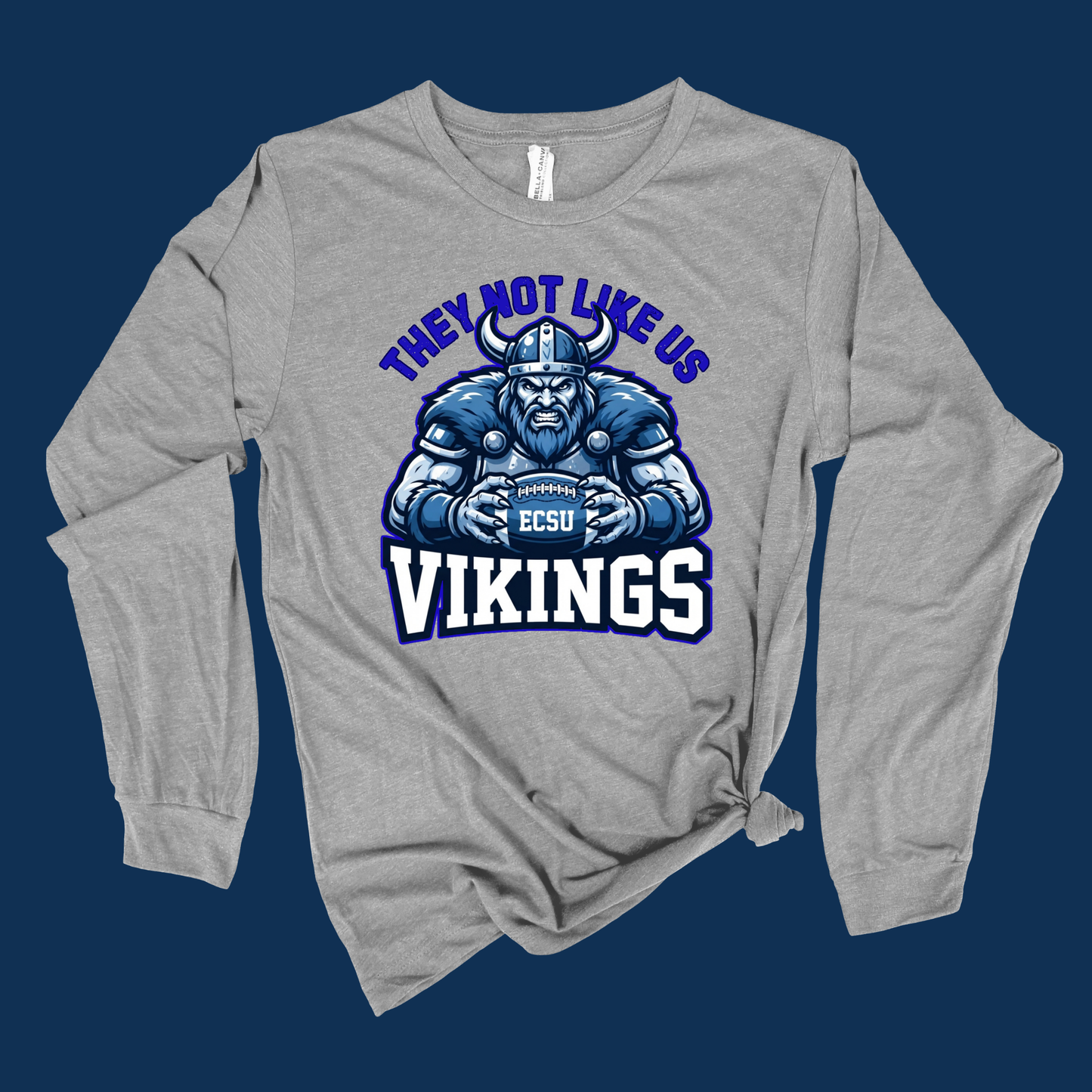 A heather gray long-sleeve t-shirt with a graphic of a blue and white football player wearing a horned helmet, with the text 'THEY NOT LIKE US VIKINGS' and 'ECSU' on the front, displayed against a dark blue background.