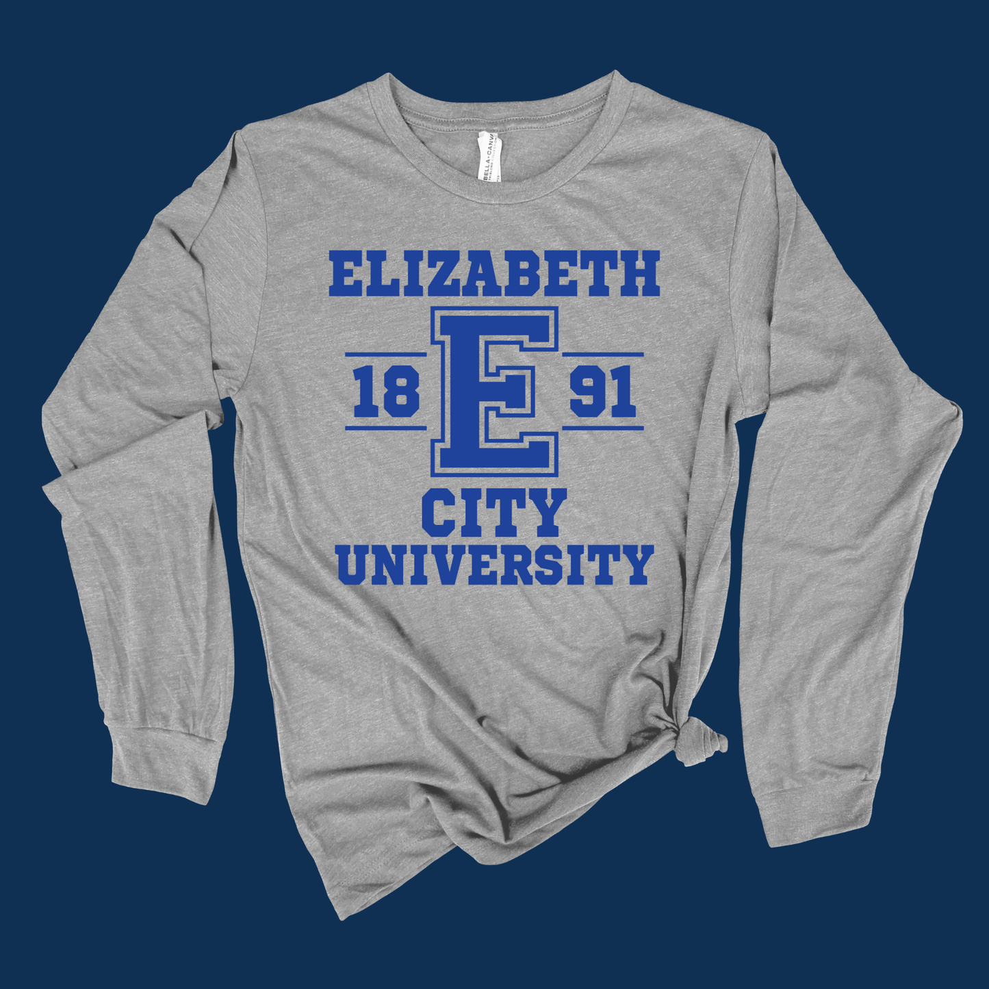 A heather gray long-sleeve t-shirt with a blue graphic print reading 'ELIZABETH 1891 CITY UNIVERSITY' on the front, styled with a knot at the bottom hem against a dark blue background.