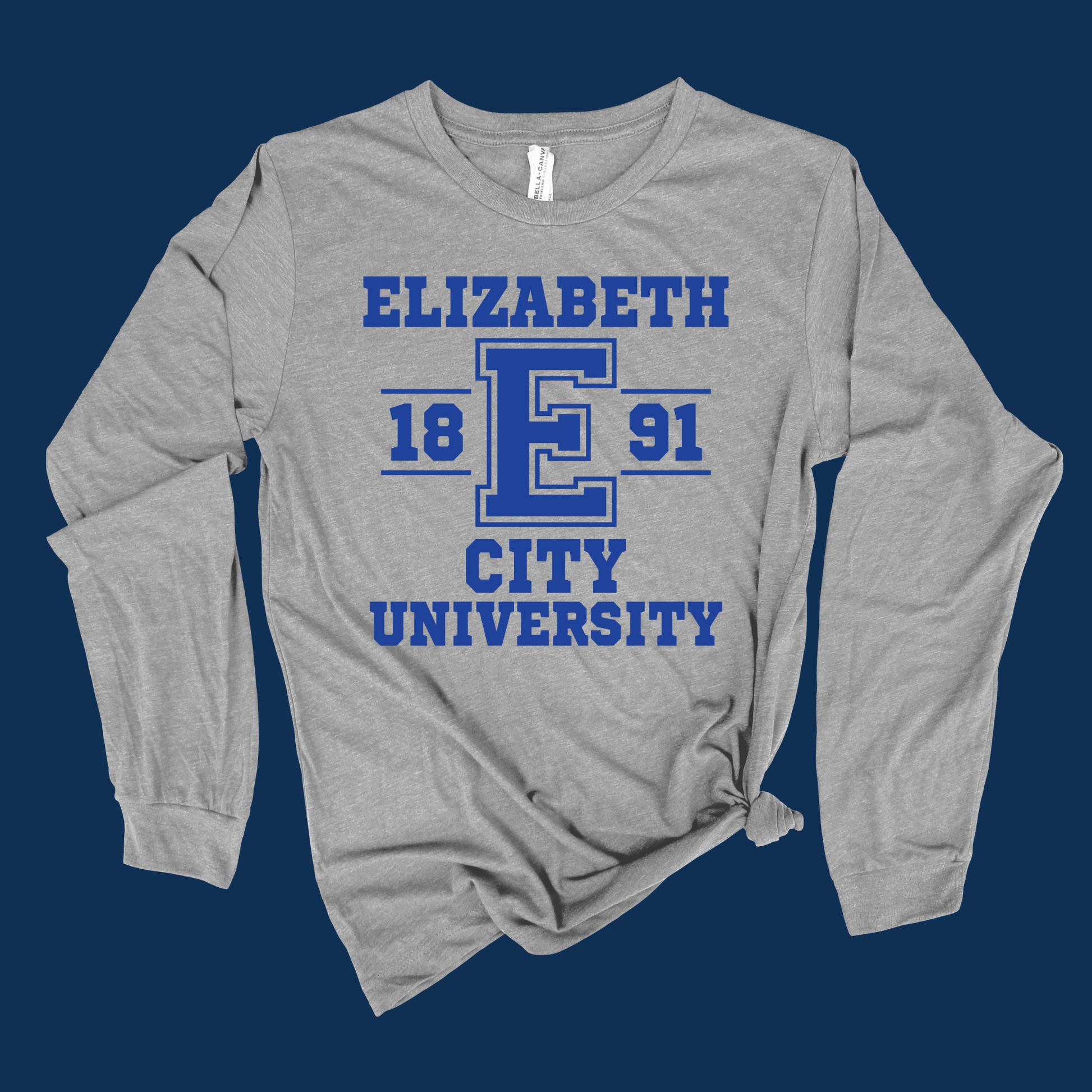 A heather gray long-sleeve t-shirt with a blue graphic print reading 'ELIZABETH 1891 CITY UNIVERSITY' on the front, styled with a knot at the bottom hem against a dark blue background.