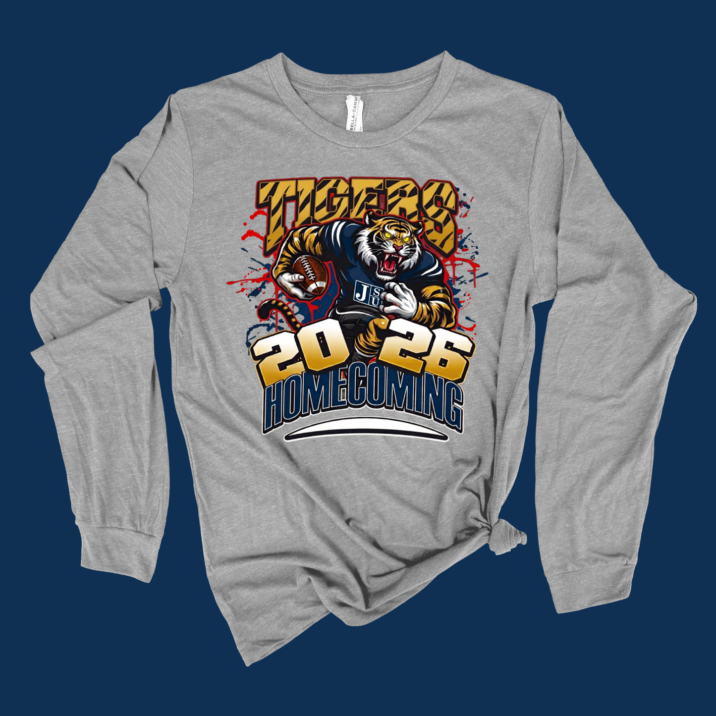 A heather gray long-sleeve t-shirt with a graphic print of a tiger mascot and the text 'TIGERS 2025 HOMECOMING' on the front, displayed against a solid dark blue background.