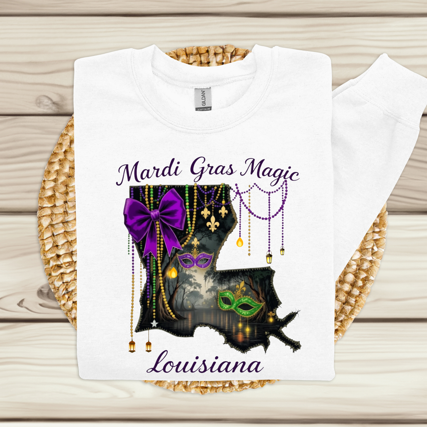White t-shirt with Mardi Gras-themed design featuring beads, a mask, and purple bow on a wooden surface.