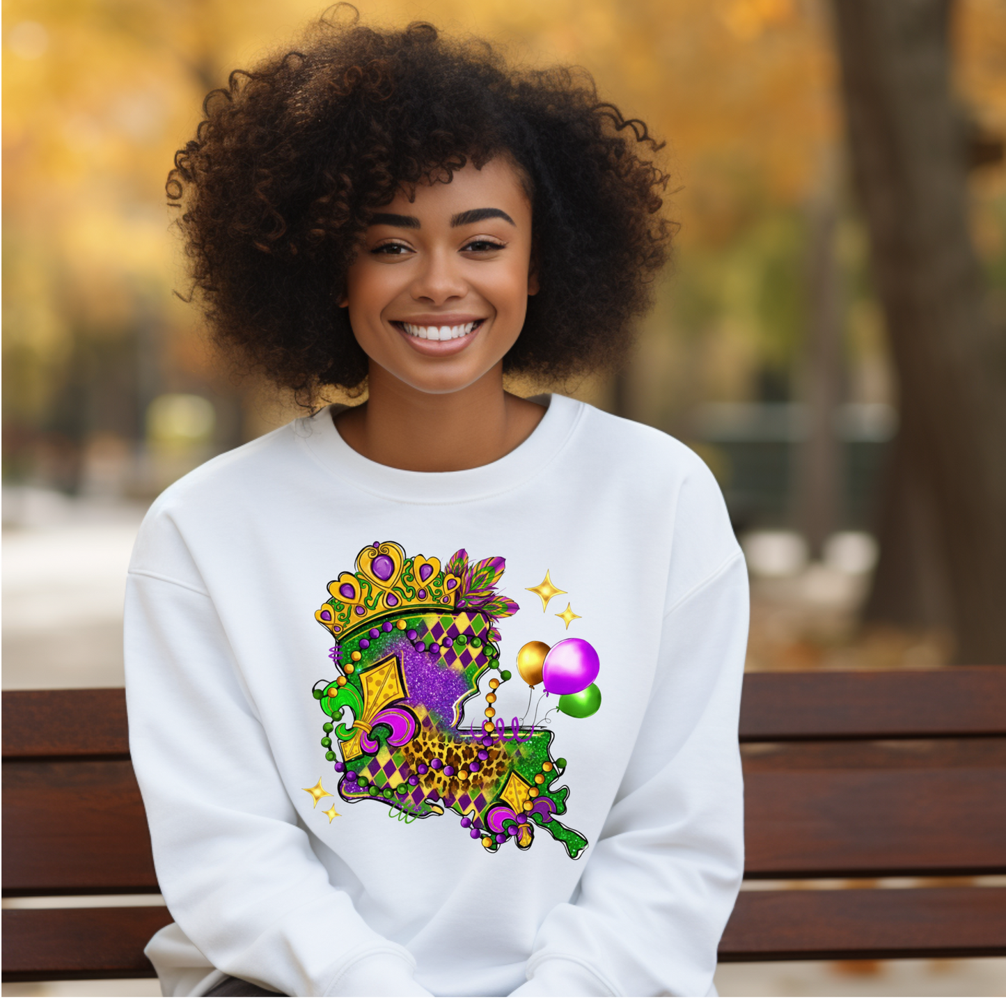 Woman wearing a white sweatshirt with a colorful design, sitting on a bench outdoors.