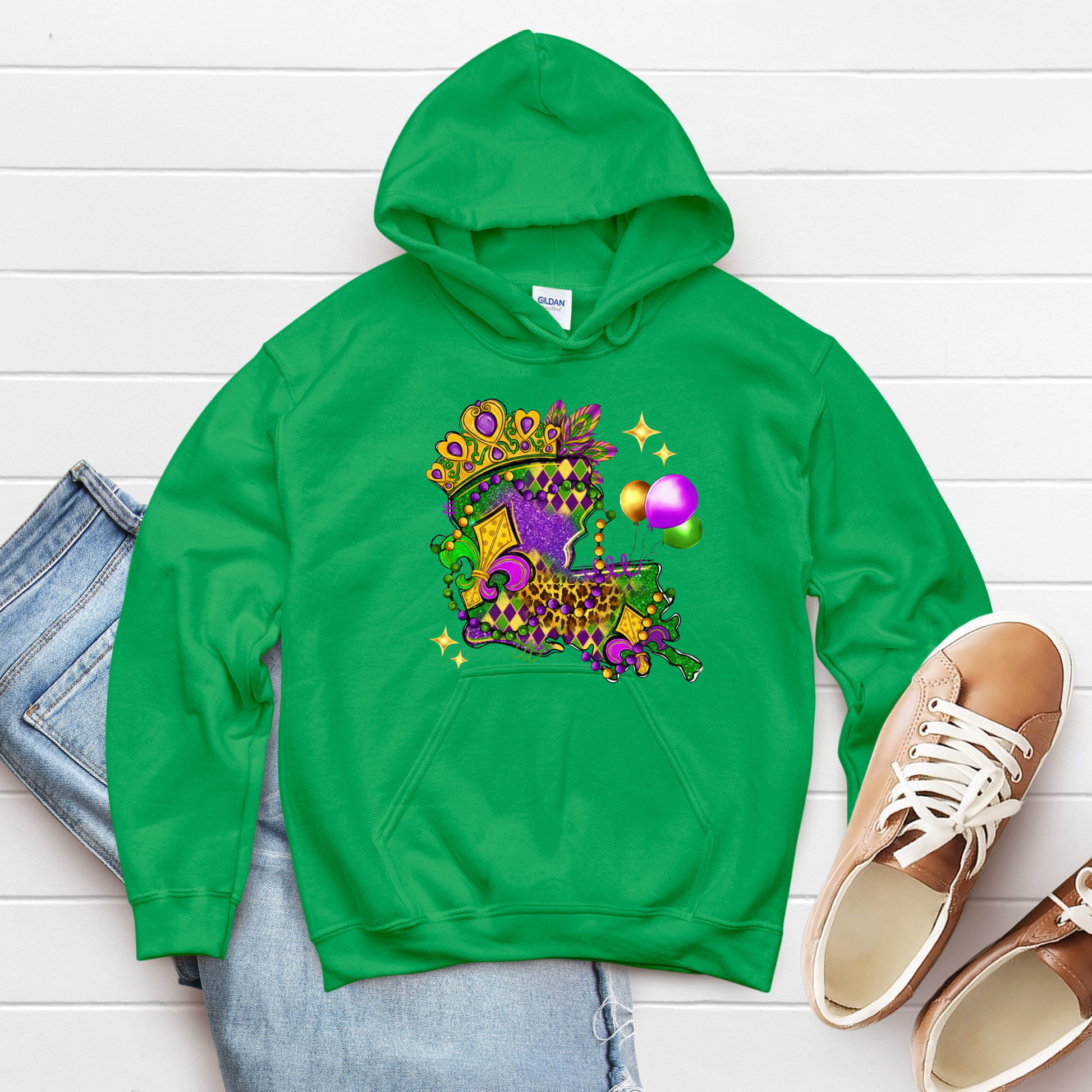 Green hoodie with festive design on a white wooden surface with jeans and shoes.