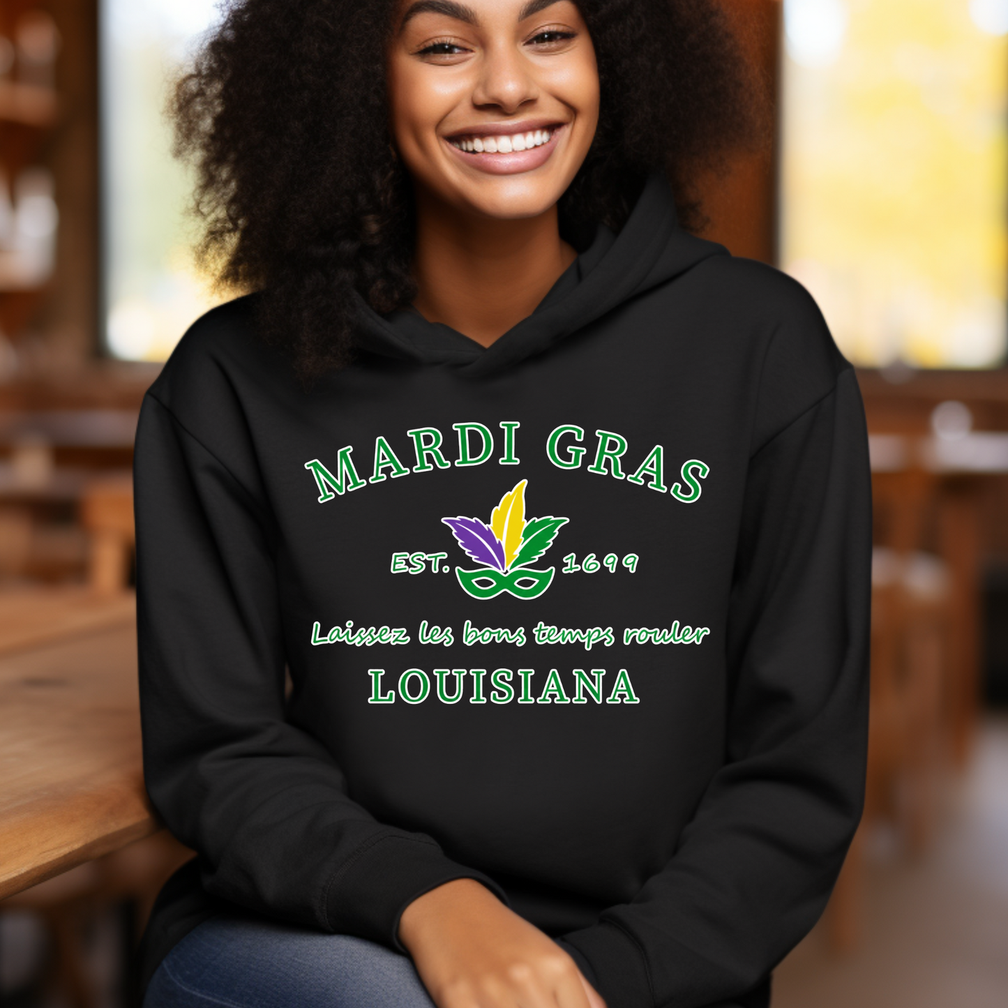 Person wearing a black hoodie with Mardi Gras-themed text and graphics, sitting indoors.