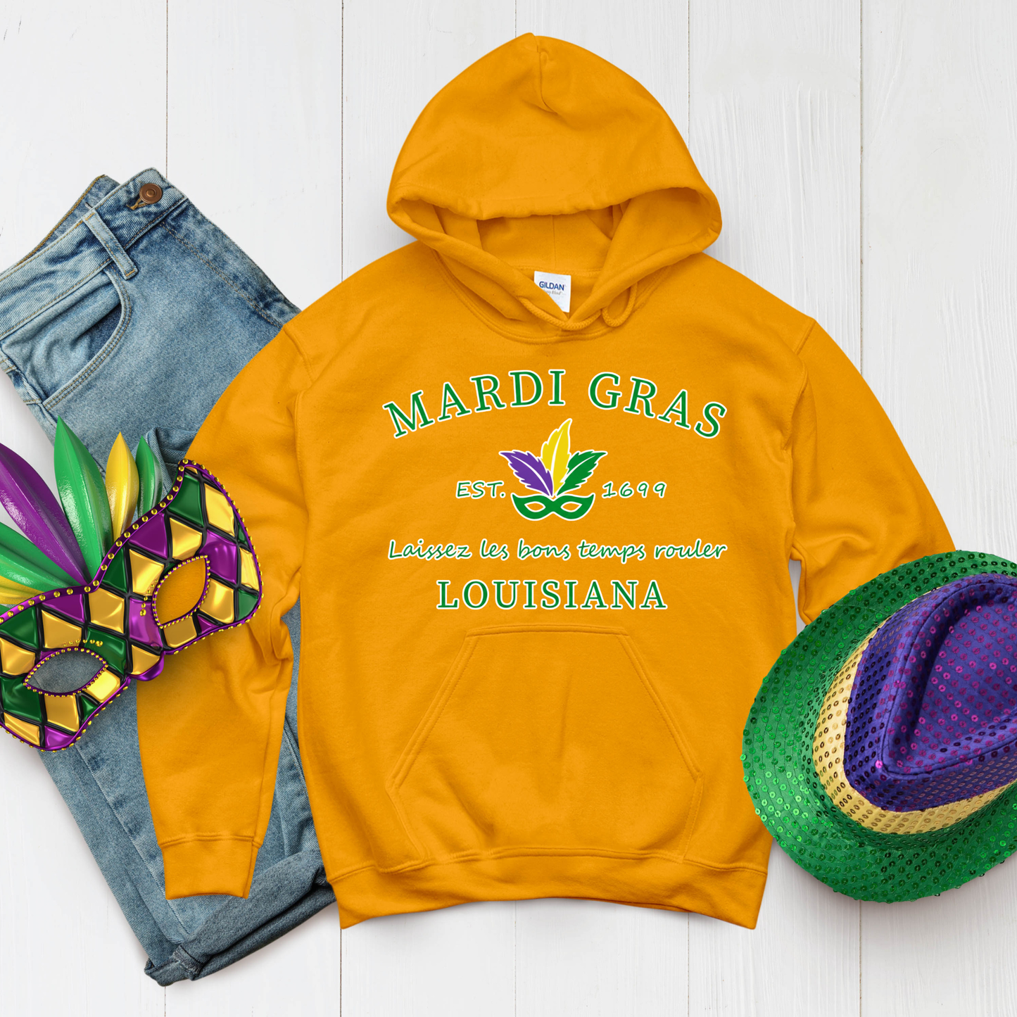 Orange hoodie with Mardi Gras-themed text and graphics on a white wooden surface.