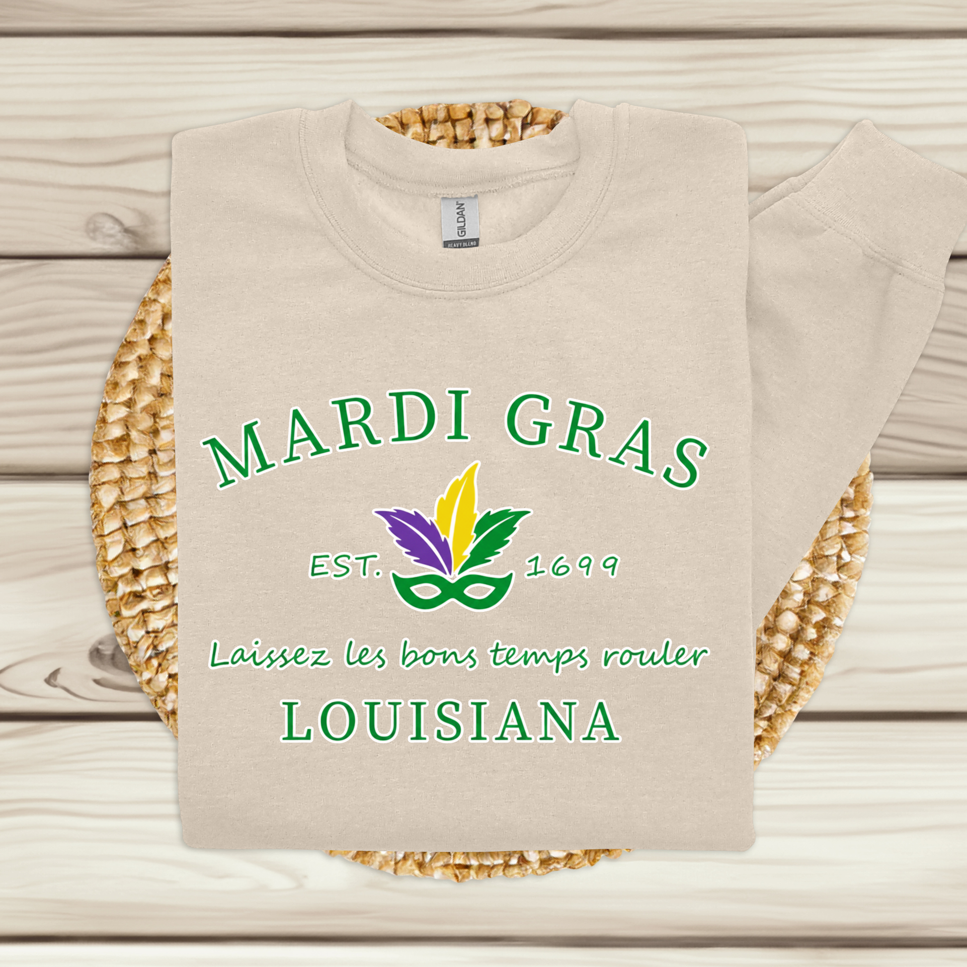 Beige sweatshirt with Mardi Gras-themed text and graphics on a woven mat.