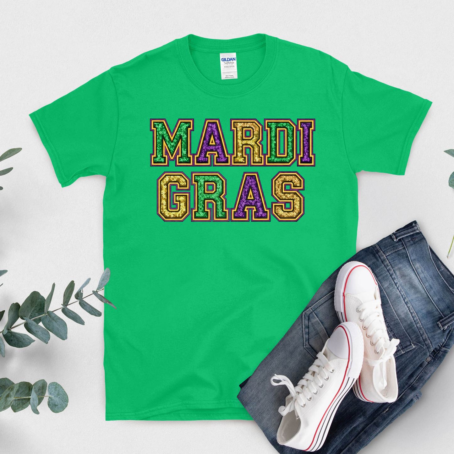 Green t-shirt with 'Mardi Gras' text, white sneakers, and jeans on a light gray background