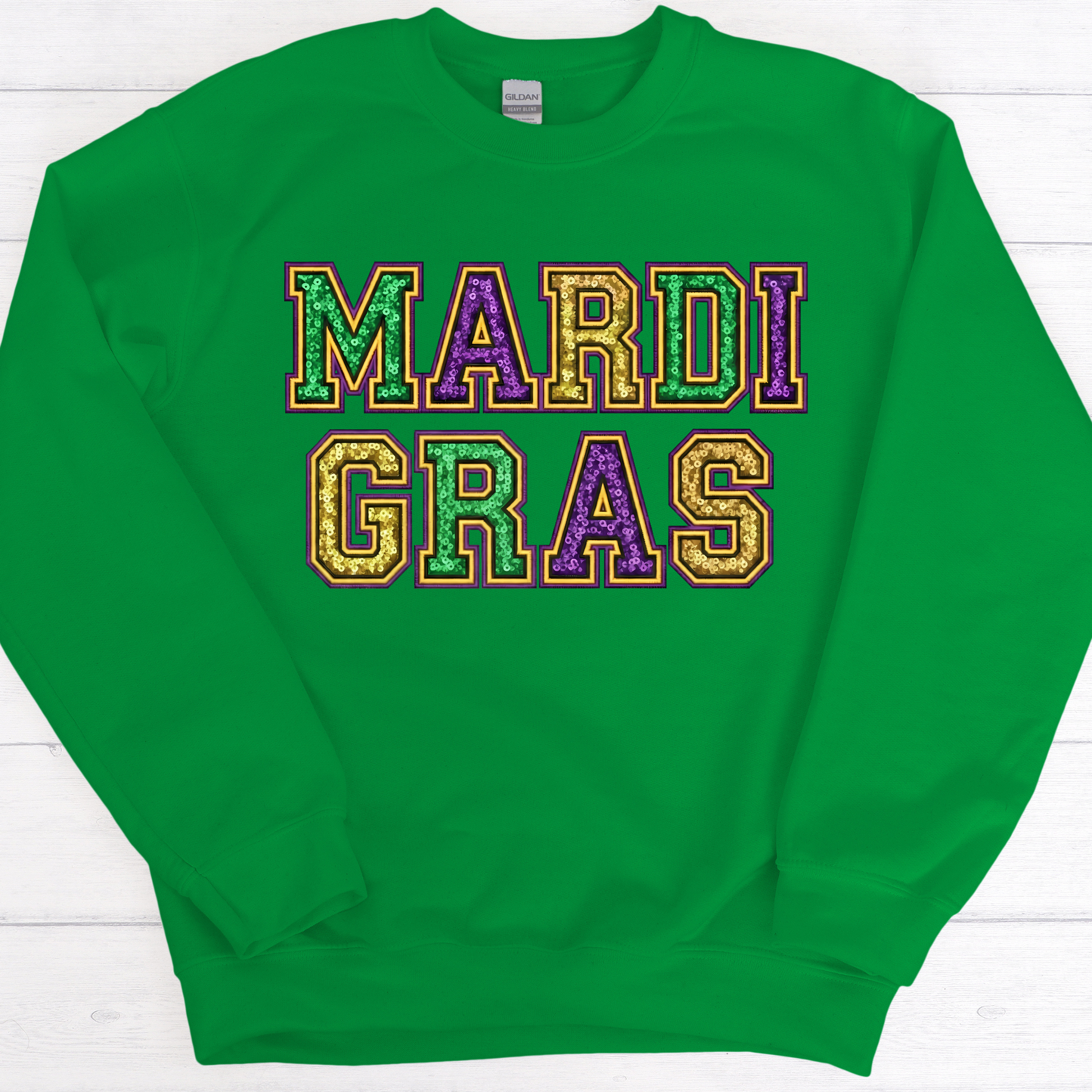 Green sweatshirt with 'MARDI GRAS' text in colorful letters on a white wooden background
