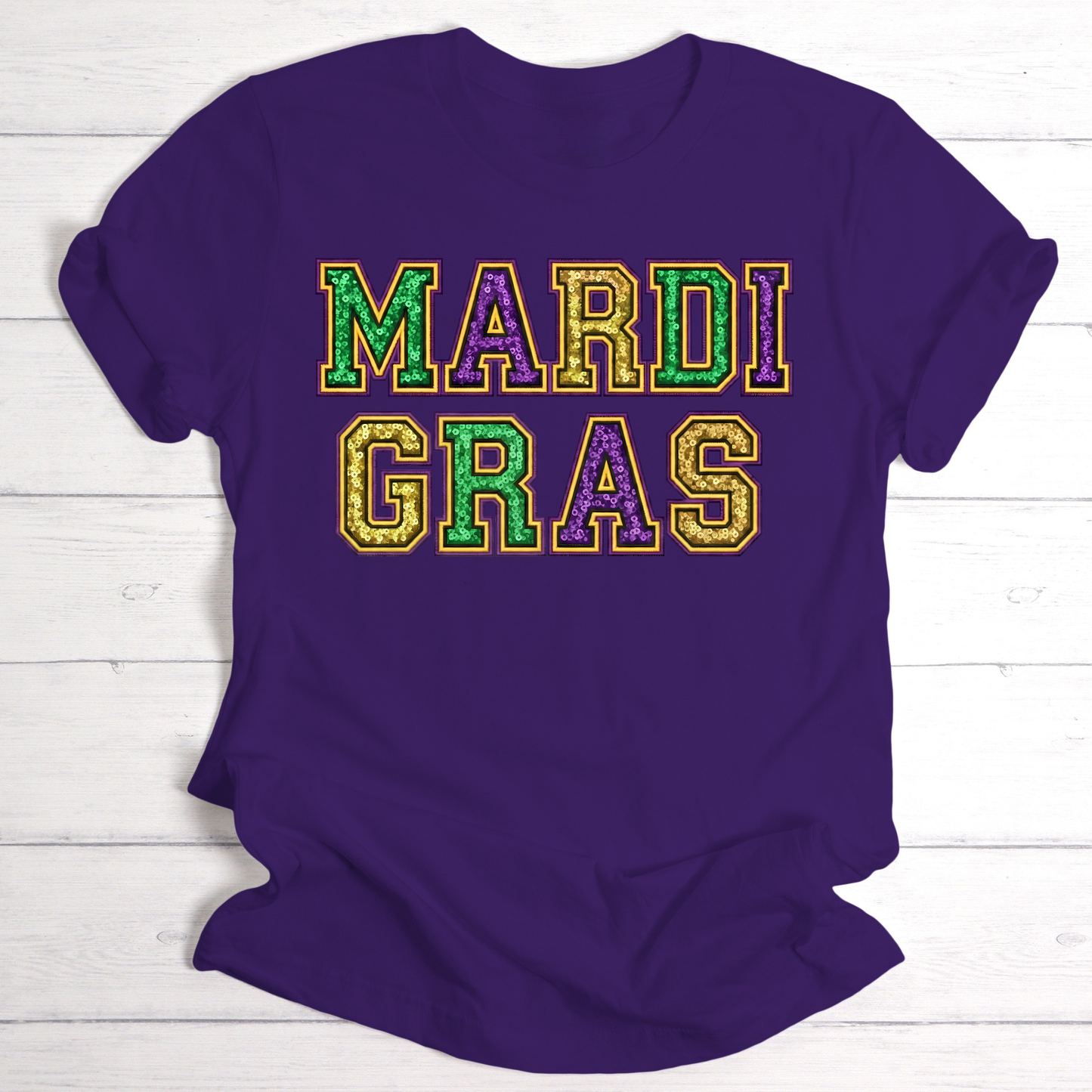 Purple t-shirt with 'MARDI GRAS' in colorful letters on a white wooden background