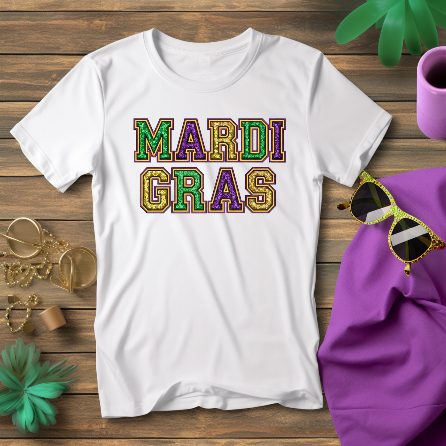 White t-shirt with 'MARDI GRAS' text on a wooden surface with sunglasses and a purple hat.