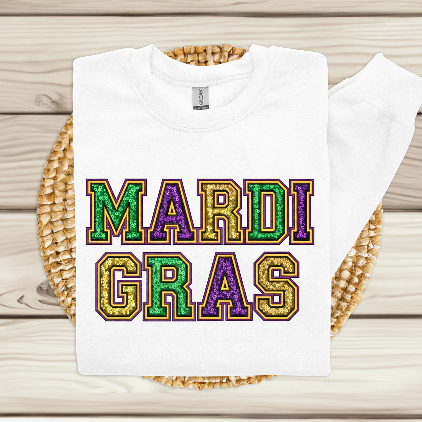White t-shirt with 'MARDI GRAS' in colorful letters on a woven mat.