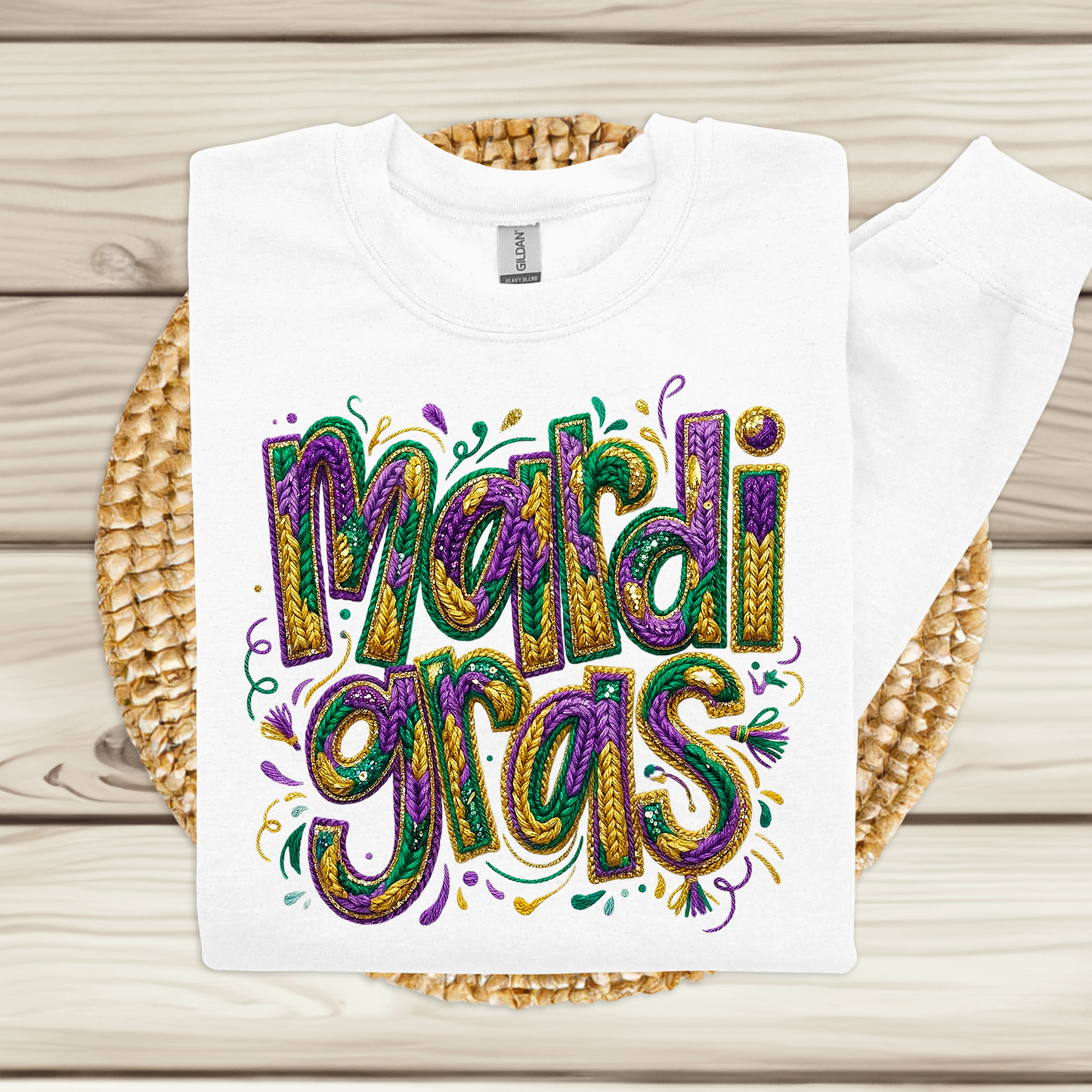 White t-shirt with colorful 'Mardi Gras' text on a woven mat.