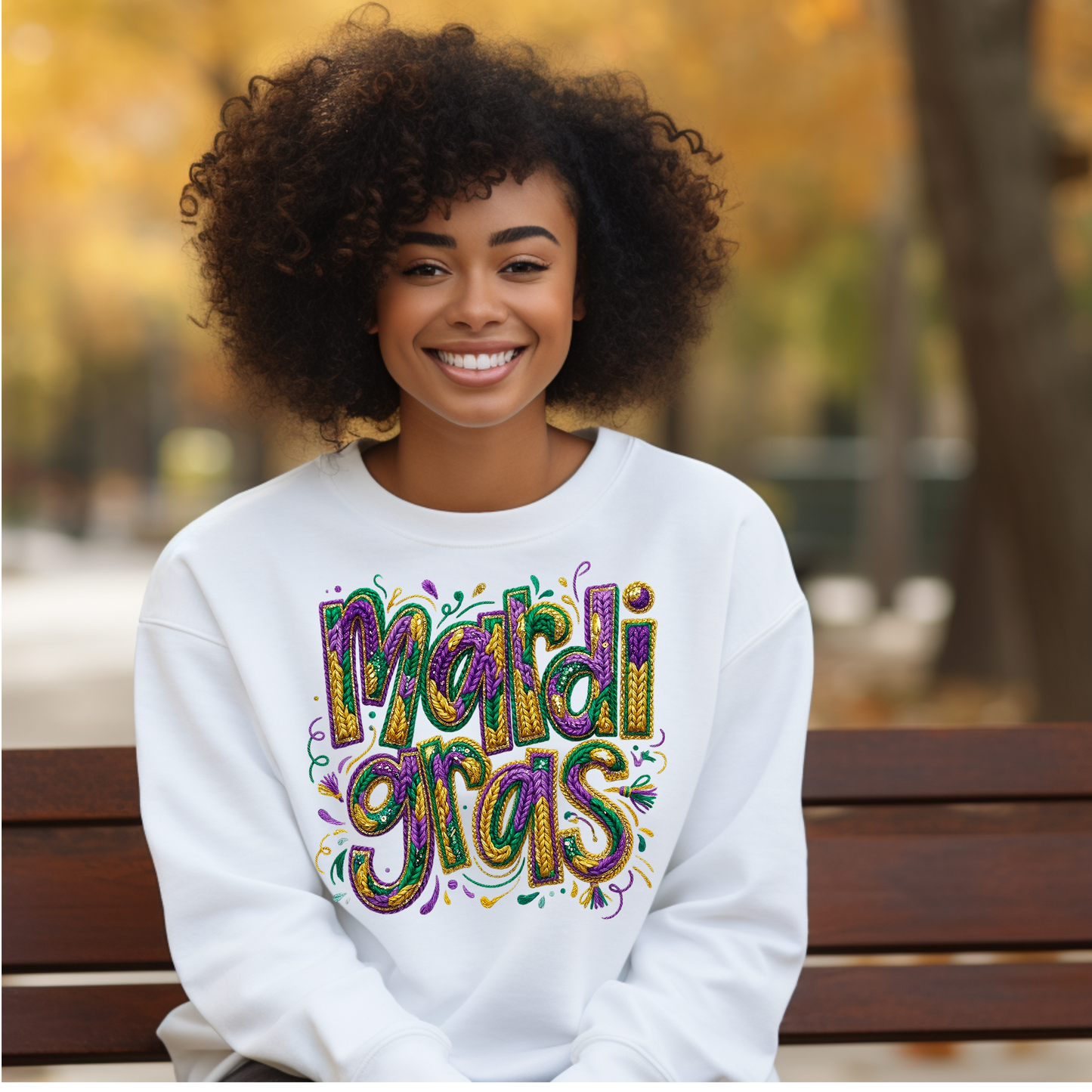 Woman wearing a white sweatshirt with 'Mardi Gras' text, sitting on a bench outdoors.