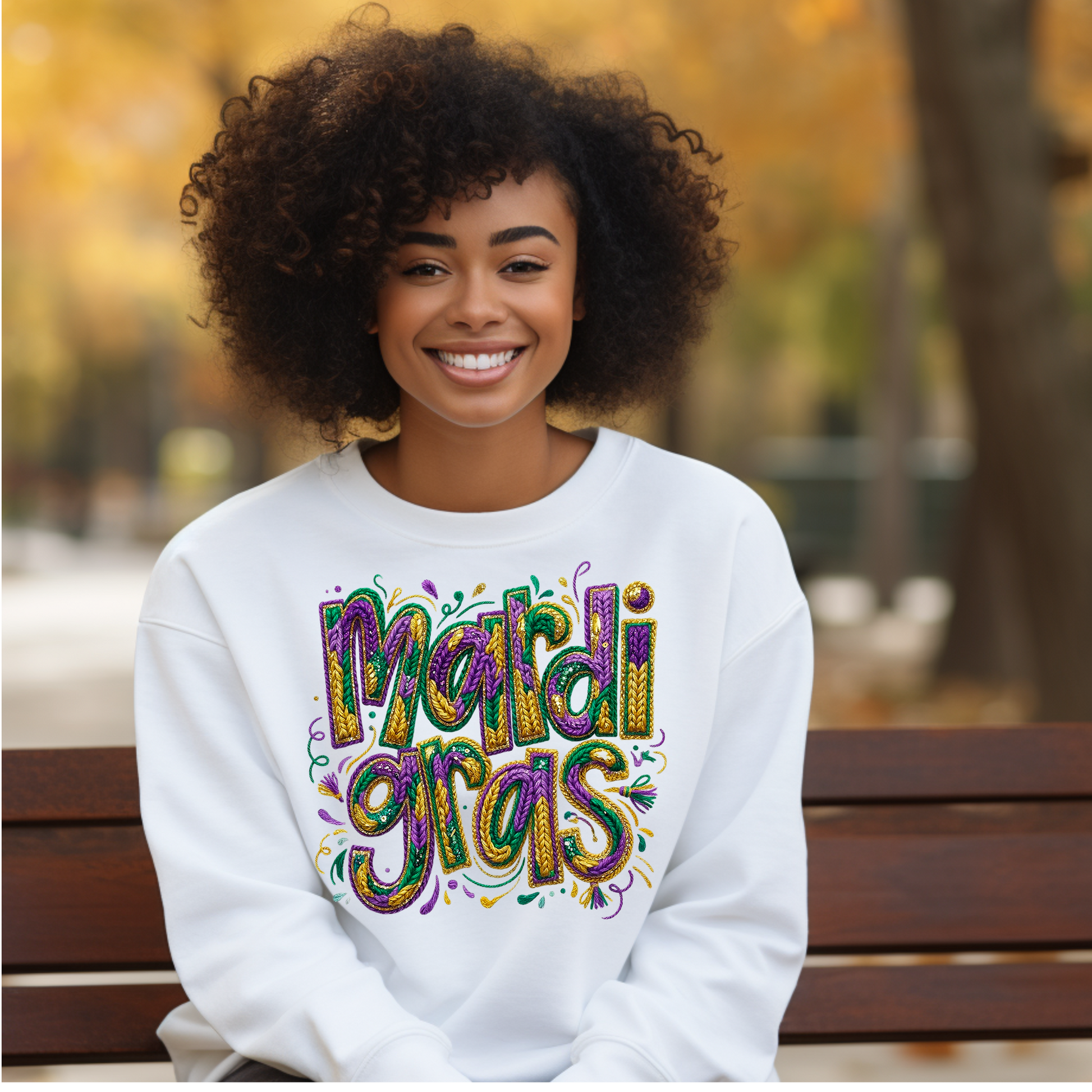 Woman wearing a white sweatshirt with 'Mardi Gras' text, sitting on a bench outdoors.