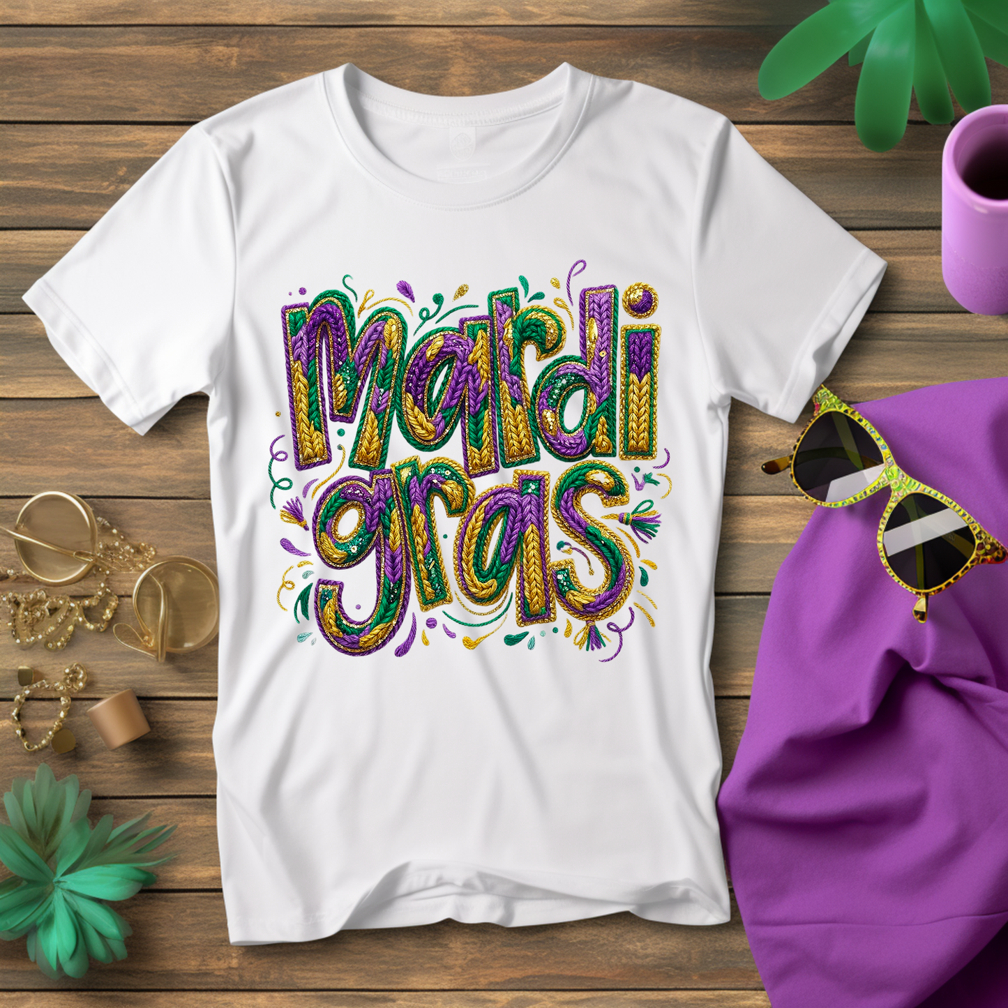 White t-shirt with 'Mardi Gras' design on a wooden surface with accessories.