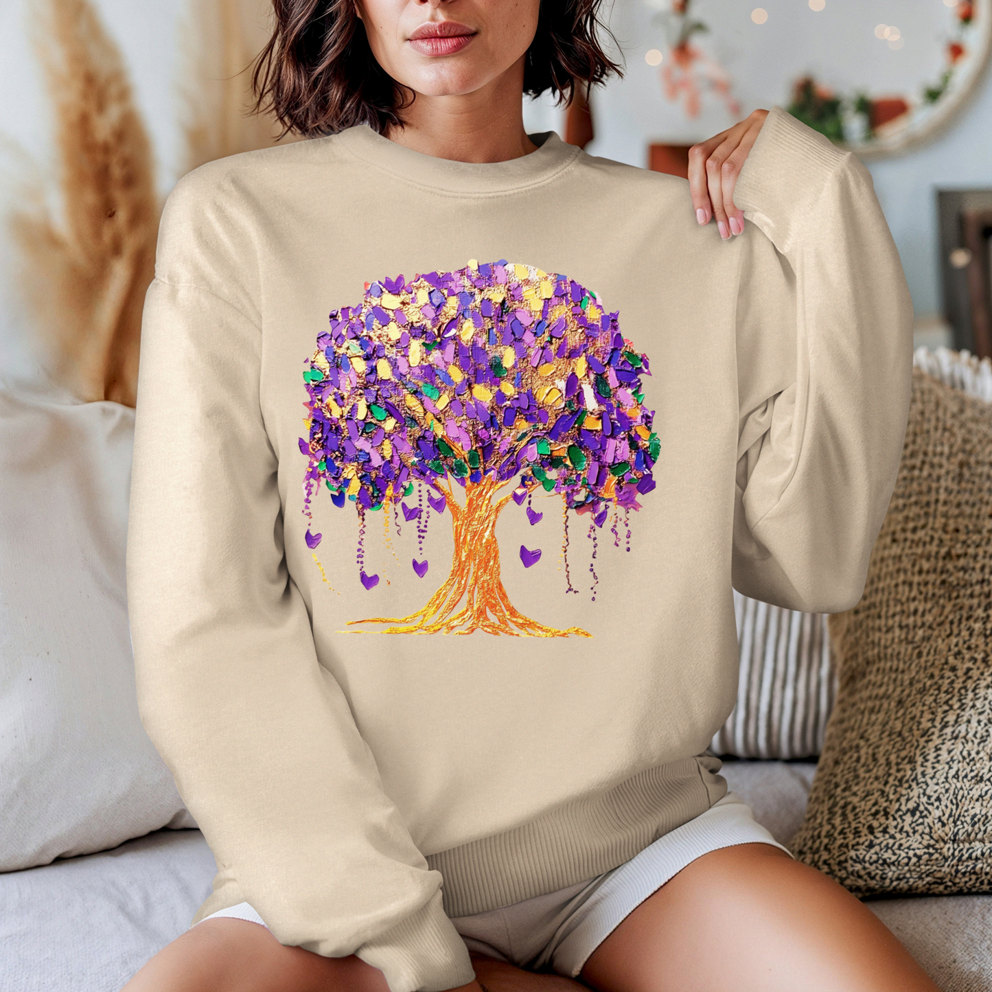 Person wearing a beige sweatshirt with a colorful tree design in a casual setting.