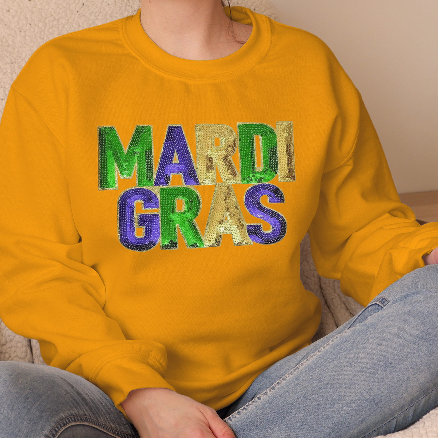 Person wearing a yellow sweatshirt with 'MARDI GRAS' in colorful letters.