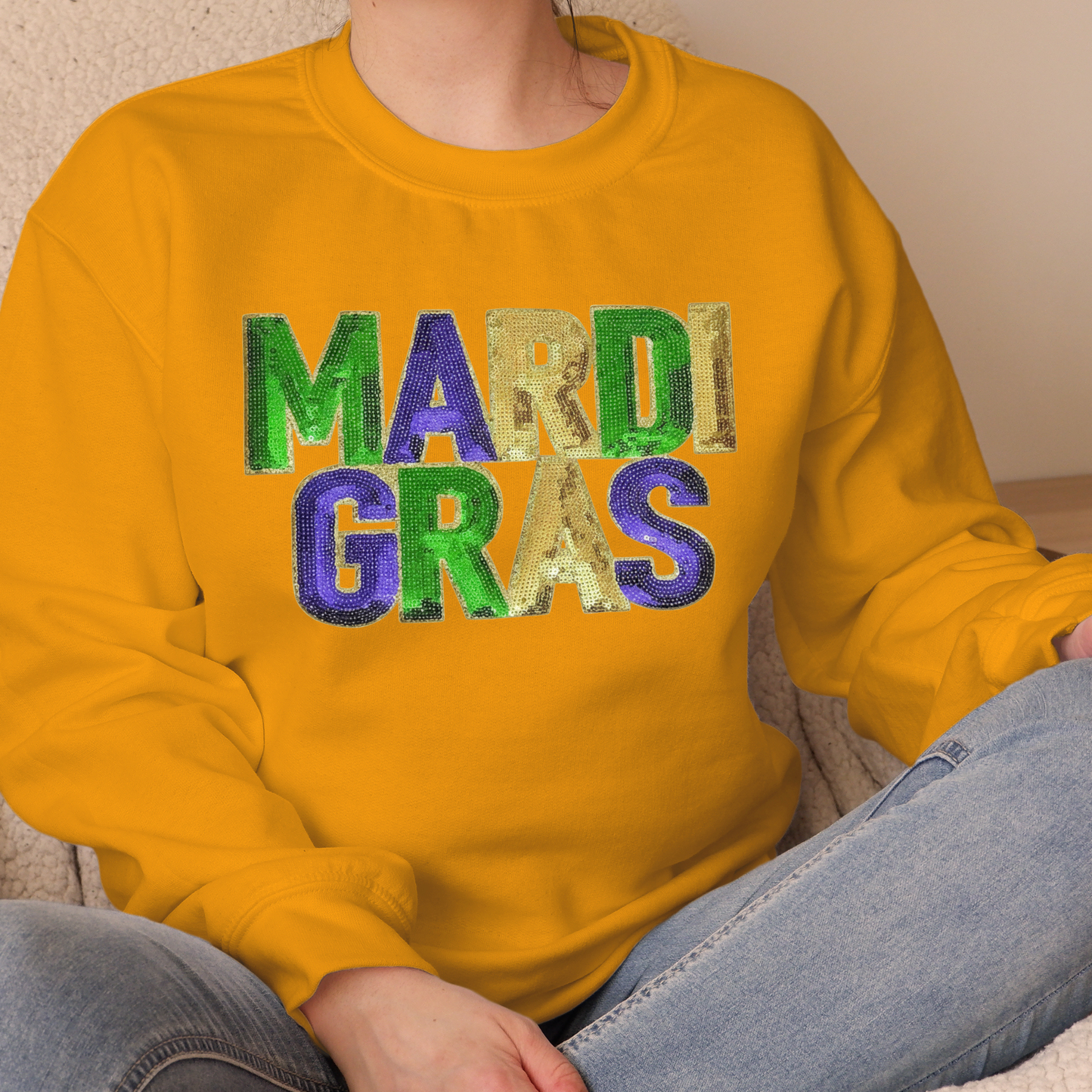 Person wearing a yellow sweatshirt with 'MARDI GRAS' in colorful letters.