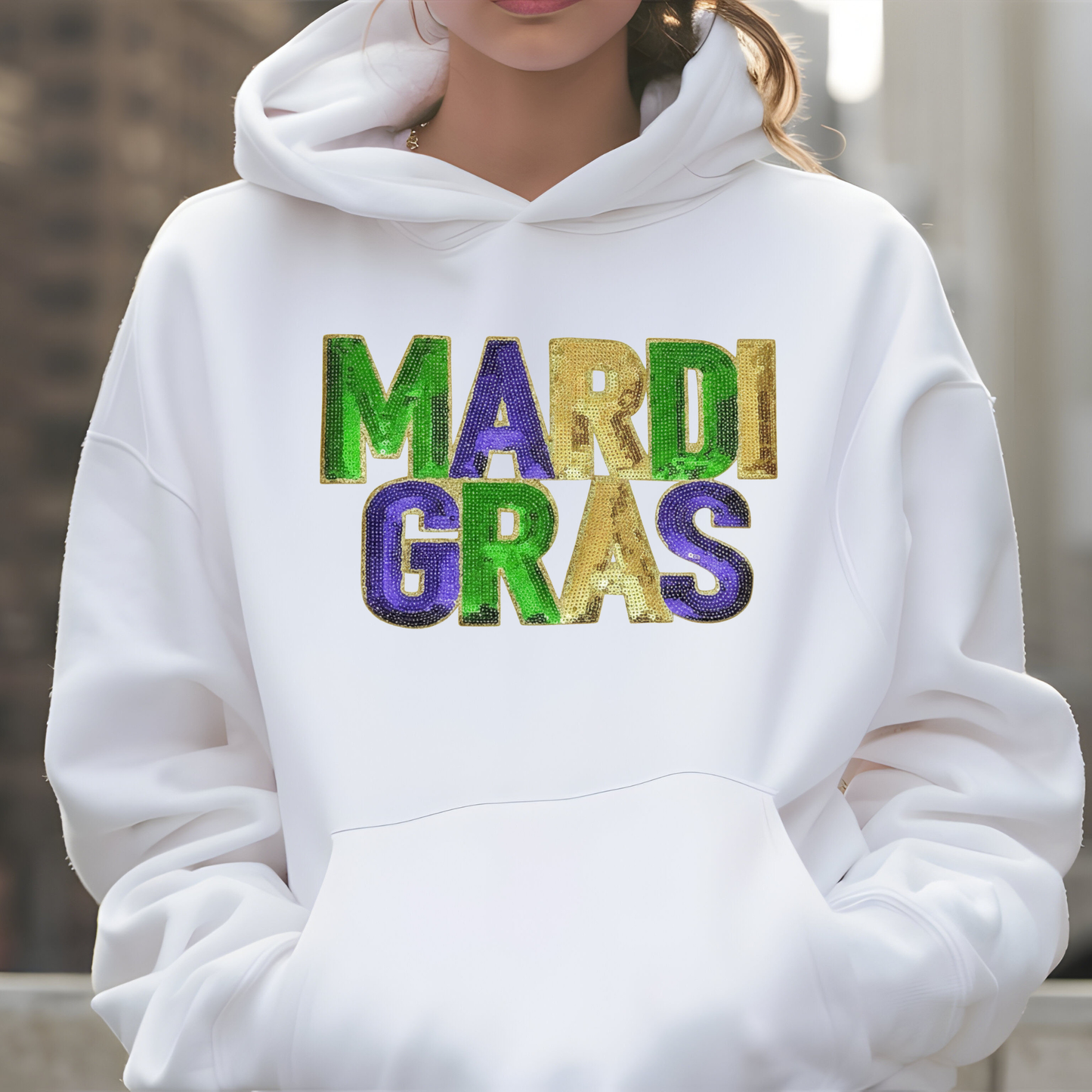 White hoodie with 'MARDI GRAS' text in colorful letters on a blurred background