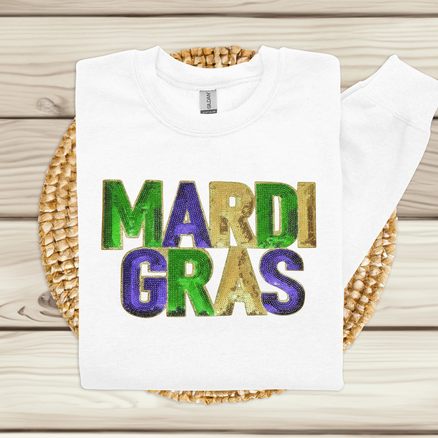 White t-shirt with 'MARDI GRAS' in colorful letters on a woven mat.