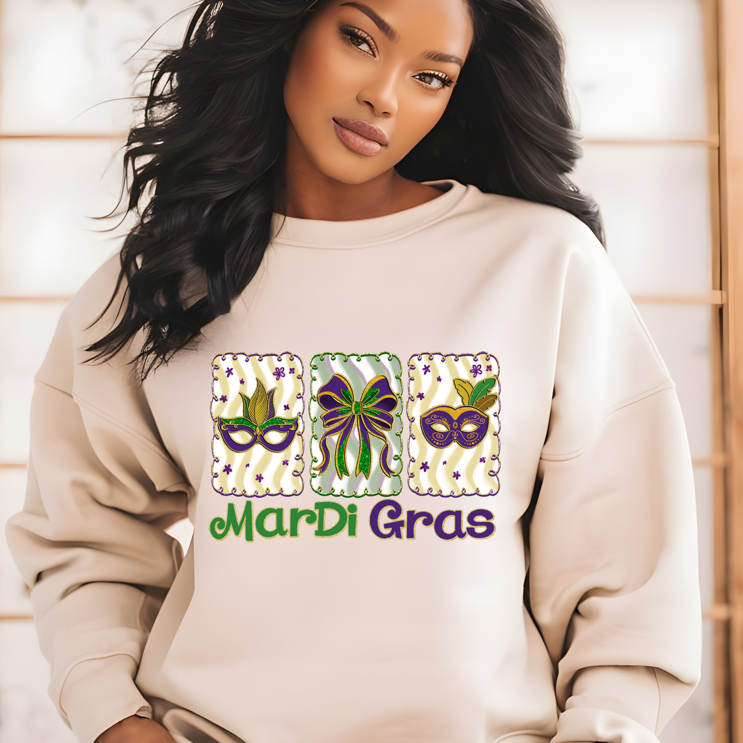 Woman wearing a beige sweatshirt with Mardi Gras-themed designs and text.