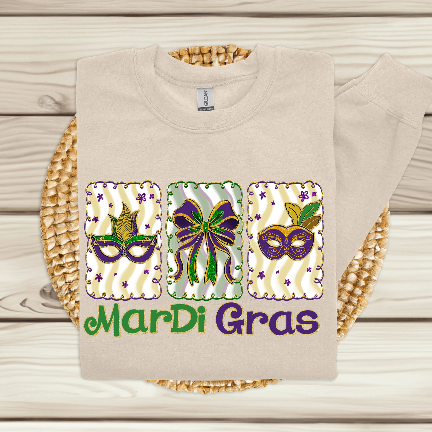 Beige t-shirt with Mardi Gras-themed design featuring masks and a bow on a wooden surface.