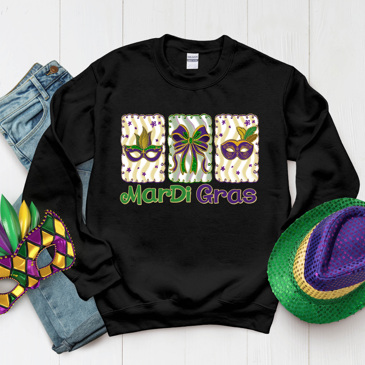 Black sweatshirt with Mardi Gras-themed design on a white surface with Mardi Gras accessories.