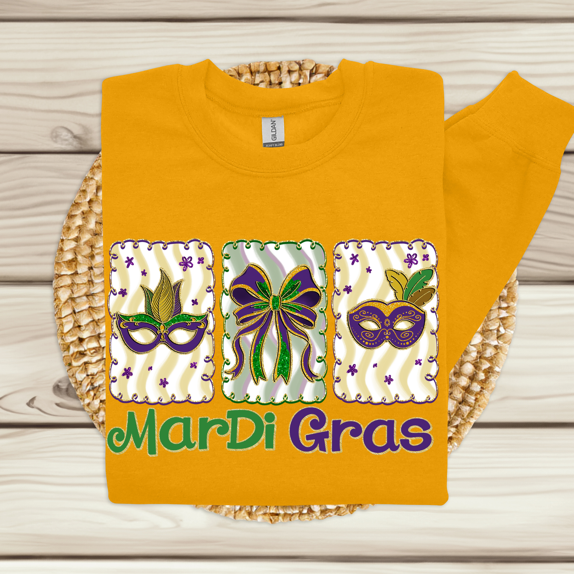 Yellow t-shirt with Mardi Gras-themed design featuring masks and a bow on a wooden surface.