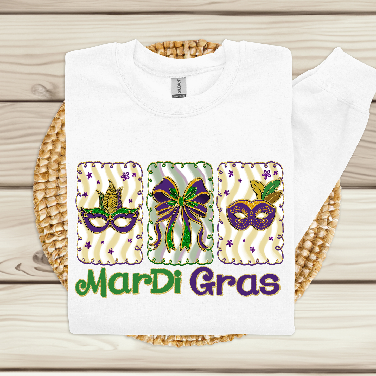 White t-shirt with Mardi Gras-themed design featuring masks and a bow on a wooden surface.