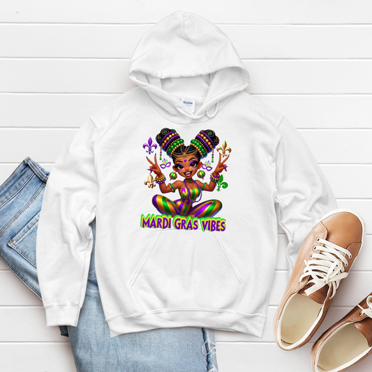 White hoodie with Mardi Gras-themed design on a white wooden surface with jeans and shoes.