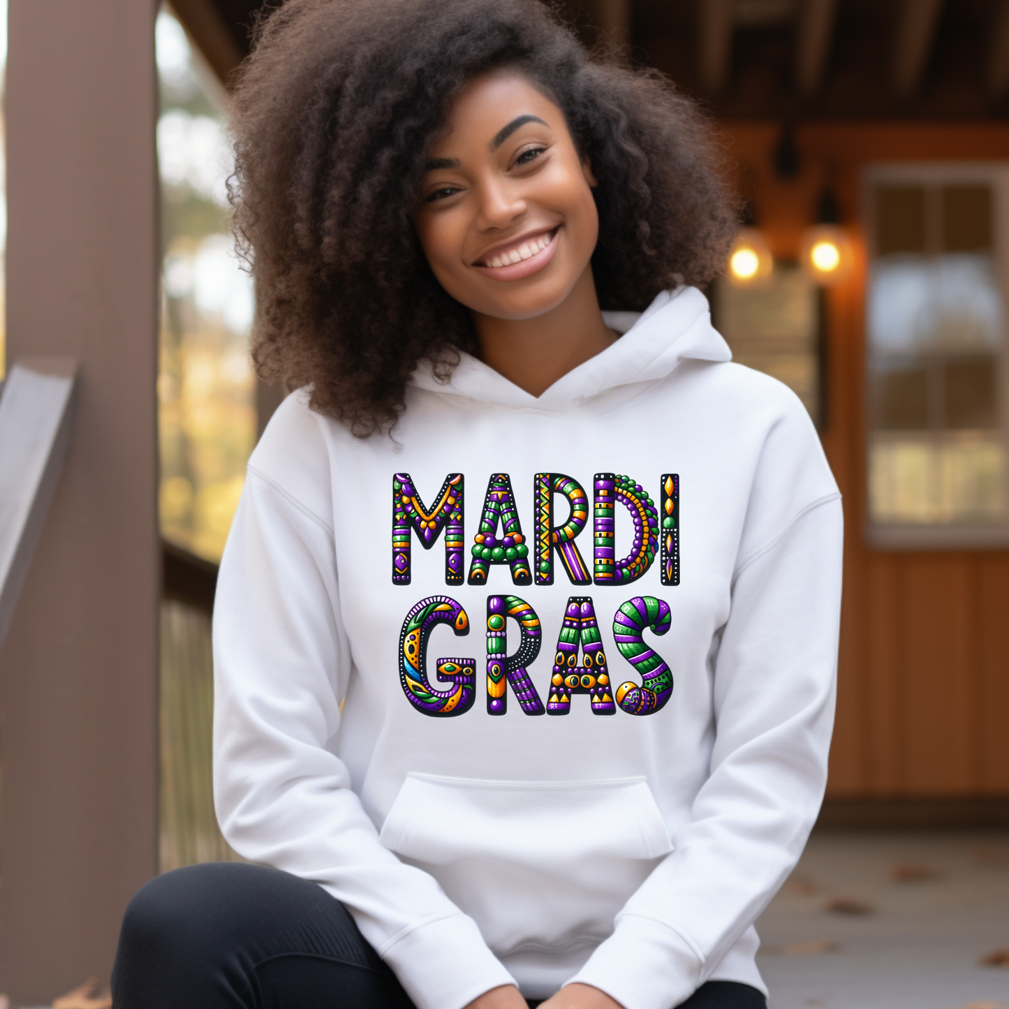 Person wearing a white hoodie with 'Mardi Gras' text, sitting outdoors.