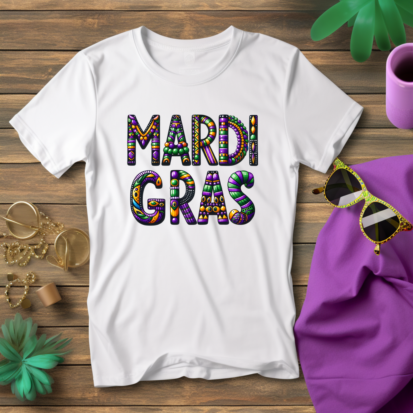 White t-shirt with 'MARDI GRAS' text on a wooden surface with sunglasses and a purple bag.