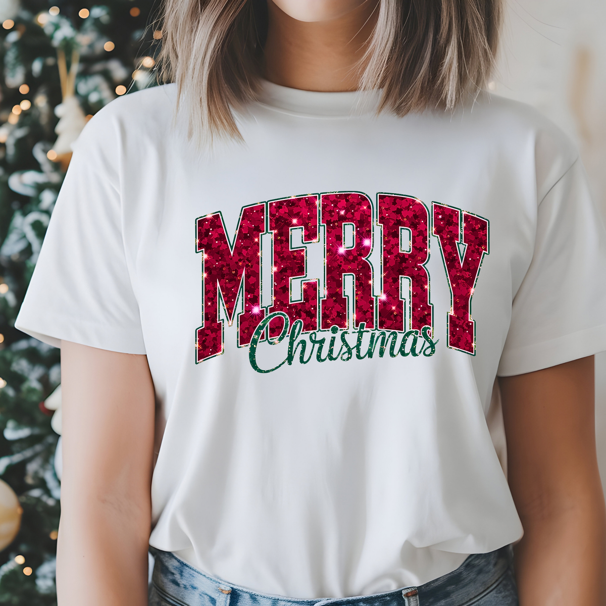 A woman wearing a white graphic t-shirt with 'MERRY Christmas' printed on the front. The word 'MERRY' is in a textured red glitter-style font with a thin green outline, and 'Christmas' is written below in green cursive.