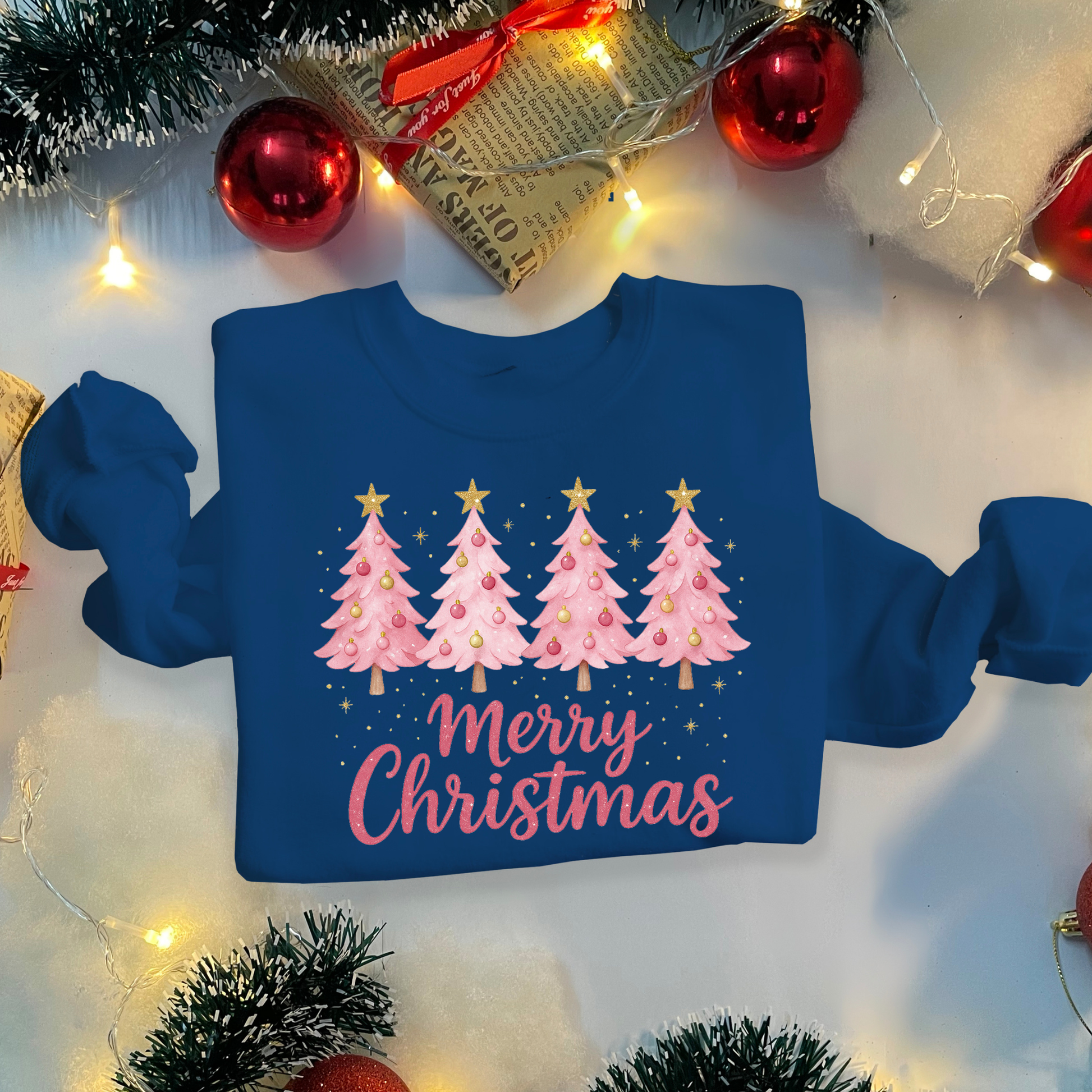 Blue sweatshirt with pink Christmas tree design and 'Merry Christmas' text, surrounded by festive decorations.
