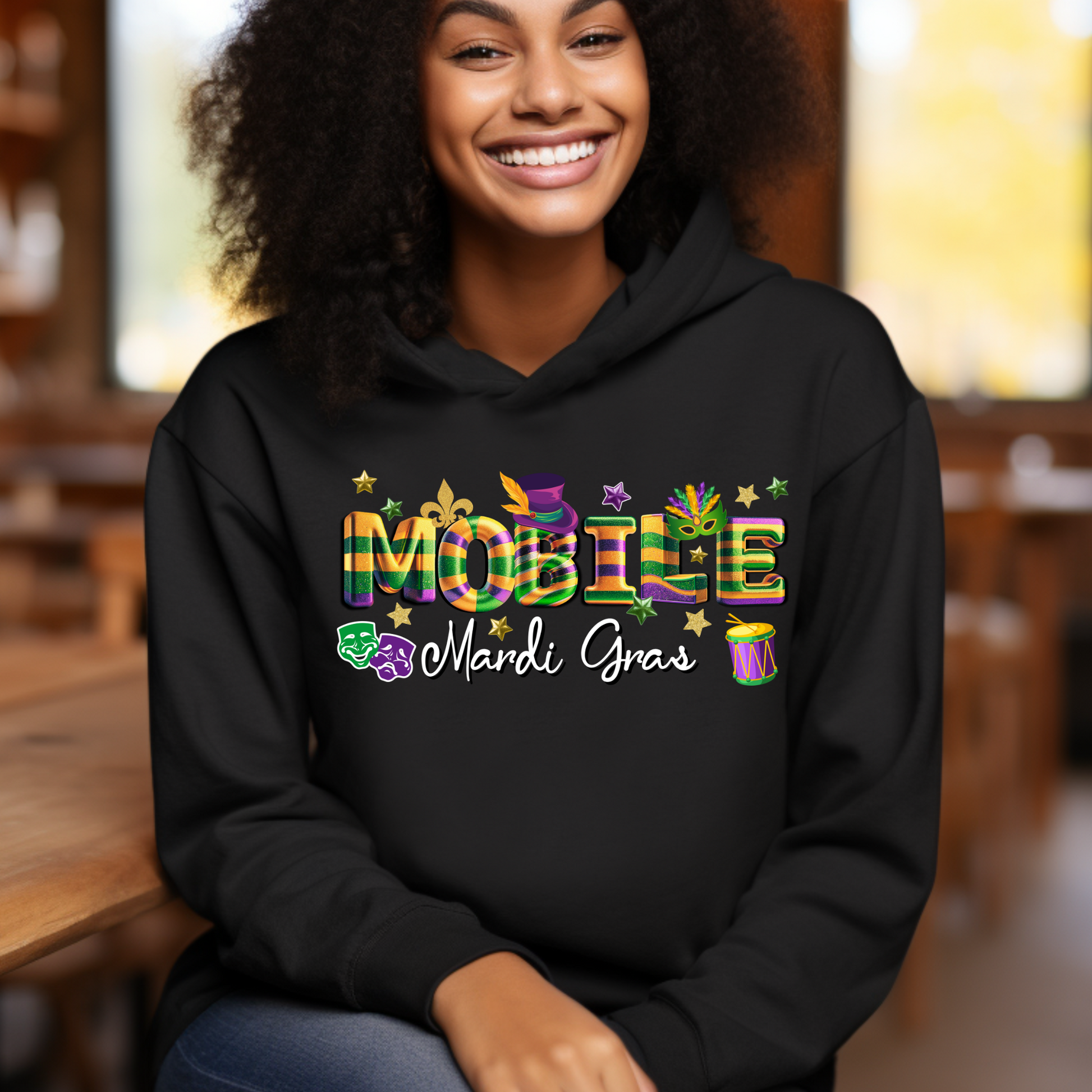 Person wearing a black hoodie with 'MOBIE Mardi Gras' text and colorful design.