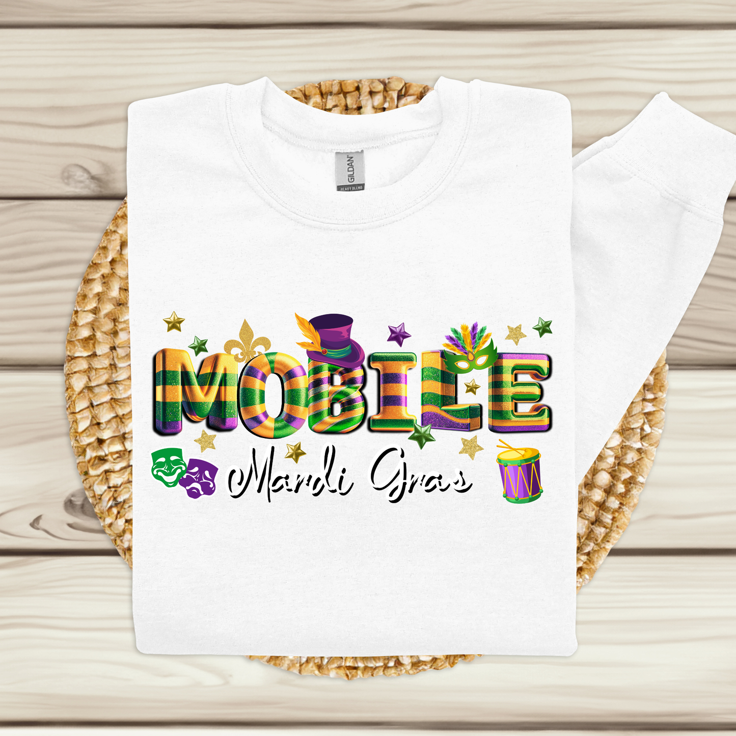 White t-shirt with colorful 'MOBILE Mardi Gras' text on a woven mat.