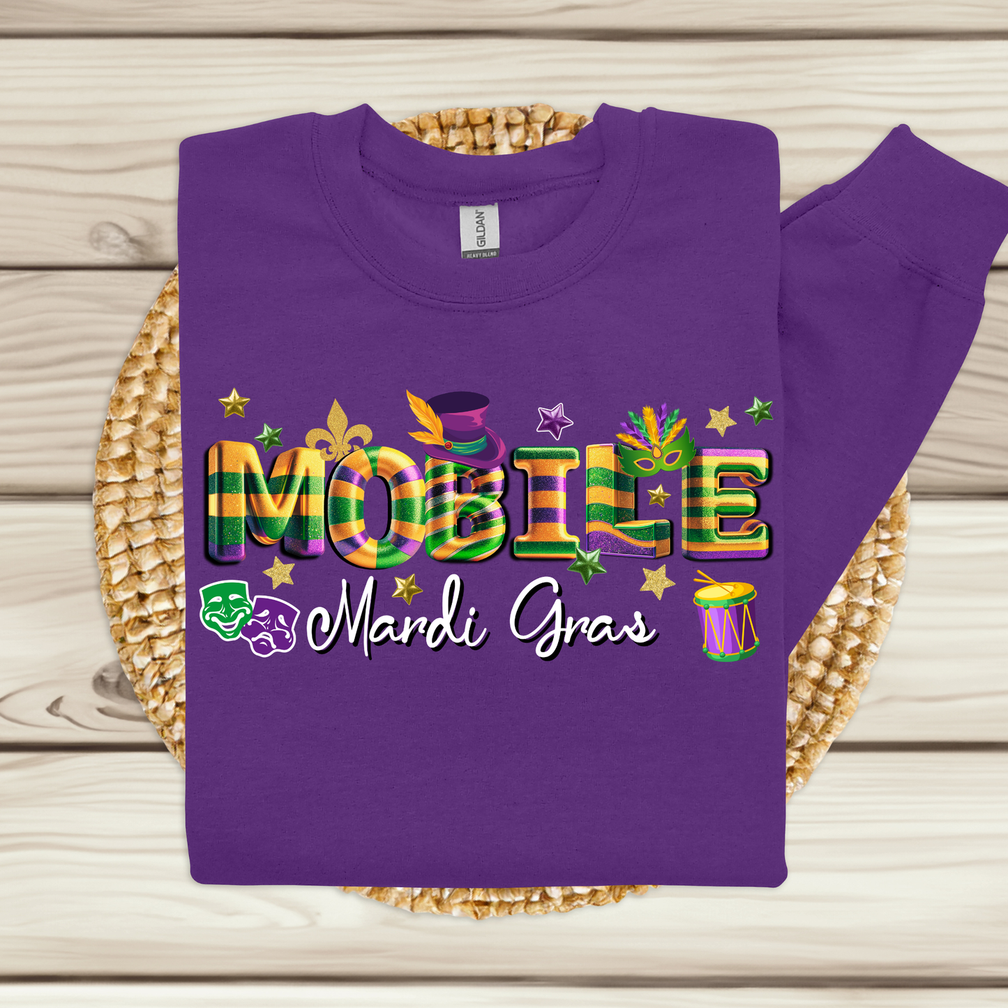 Purple sweatshirt with colorful 'MOBILE Mardi Gras' text on a woven mat.
