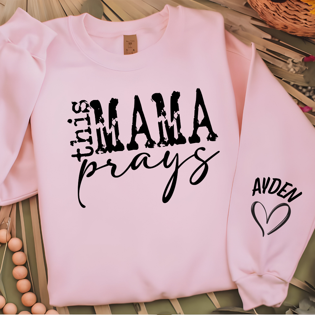 Women wearing This mama prays pink sweater emphasing a praying mama, a spiritual mama, a religious mama Sweatshirt with personalized children's name on the sleeve
