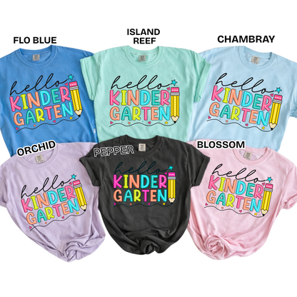 Six children's T-shirts in different colors are arranged in a 2x3 grid on a white background, each with a custom 'hello KINDER GARTEN' graphic printed on the front. Color names and shirt codes are labeled above each shirt: FLO BLUE, ISLAND REEF, CHAMBRAY, ORCHID, PEPPER, and BLOSSOM.