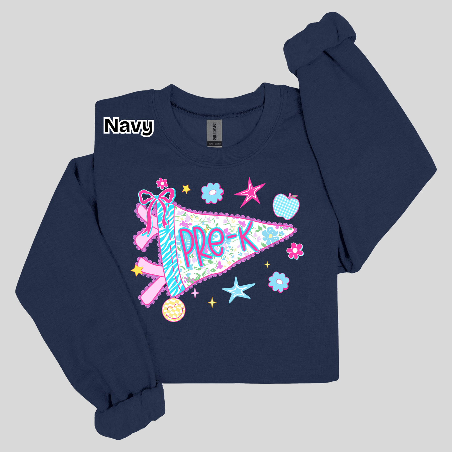 A navy blue long-sleeve sweatshirt with a colorful 'PRE-K' pennant graphic on the front, featuring a ribbon, stars, and flowers. The brand 'Gildan' is visible on the inner neck label, and a 'Navy' color label is overlaid on the upper left chest.
