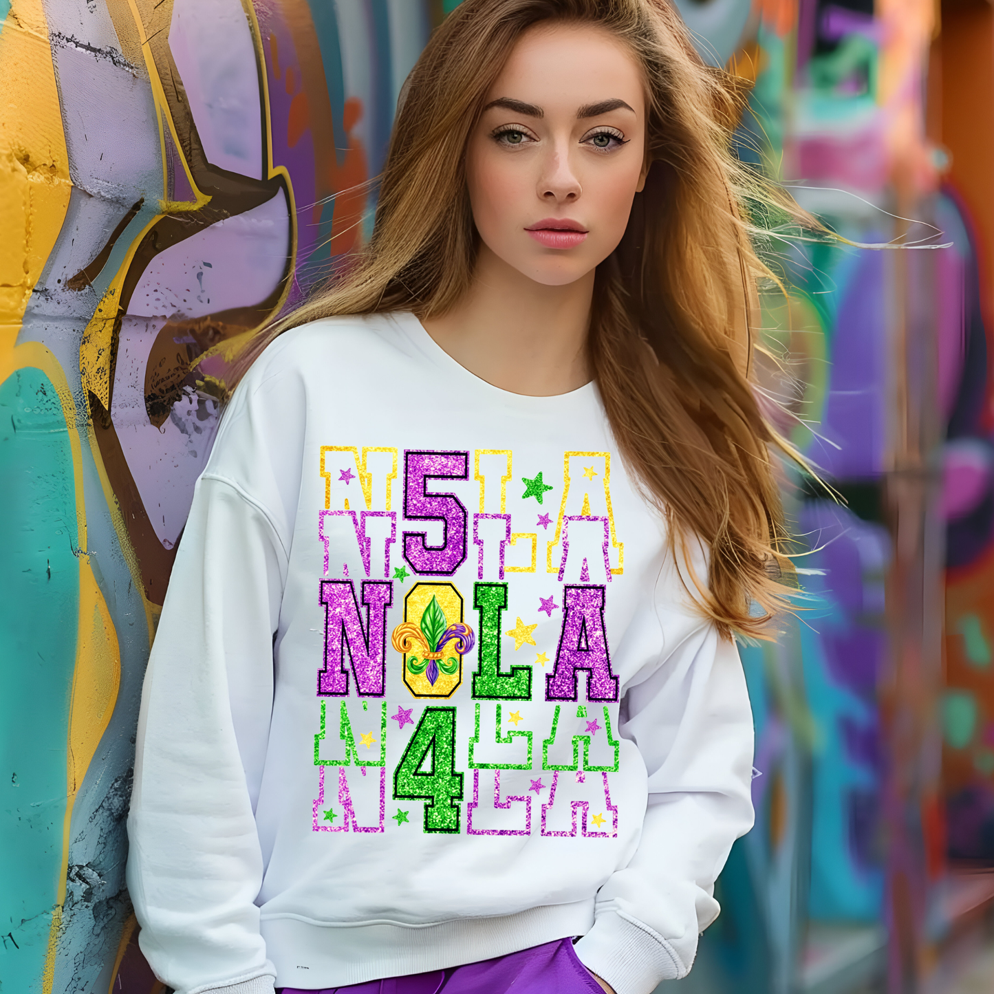 Woman wearing a colorful 'NOLA' sweatshirt in front of a graffiti wall.