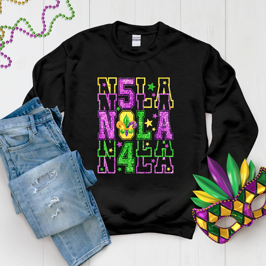 Black sweatshirt with 'NOLA' text, denim shorts, and Mardi Gras mask on a white background